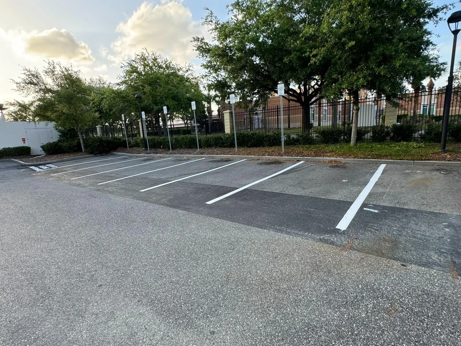 Empty outdoor parking lot with white painted spaces, trees, and a cloudy sky