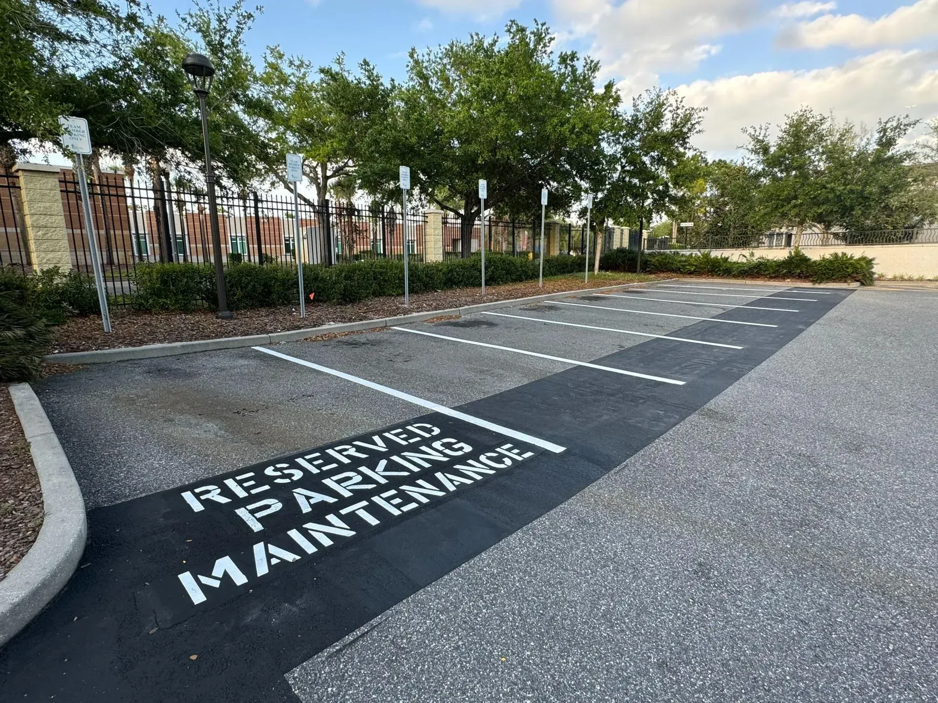 Reserved parking maintenance spaces marked on an empty paved lot near trees and a fence.