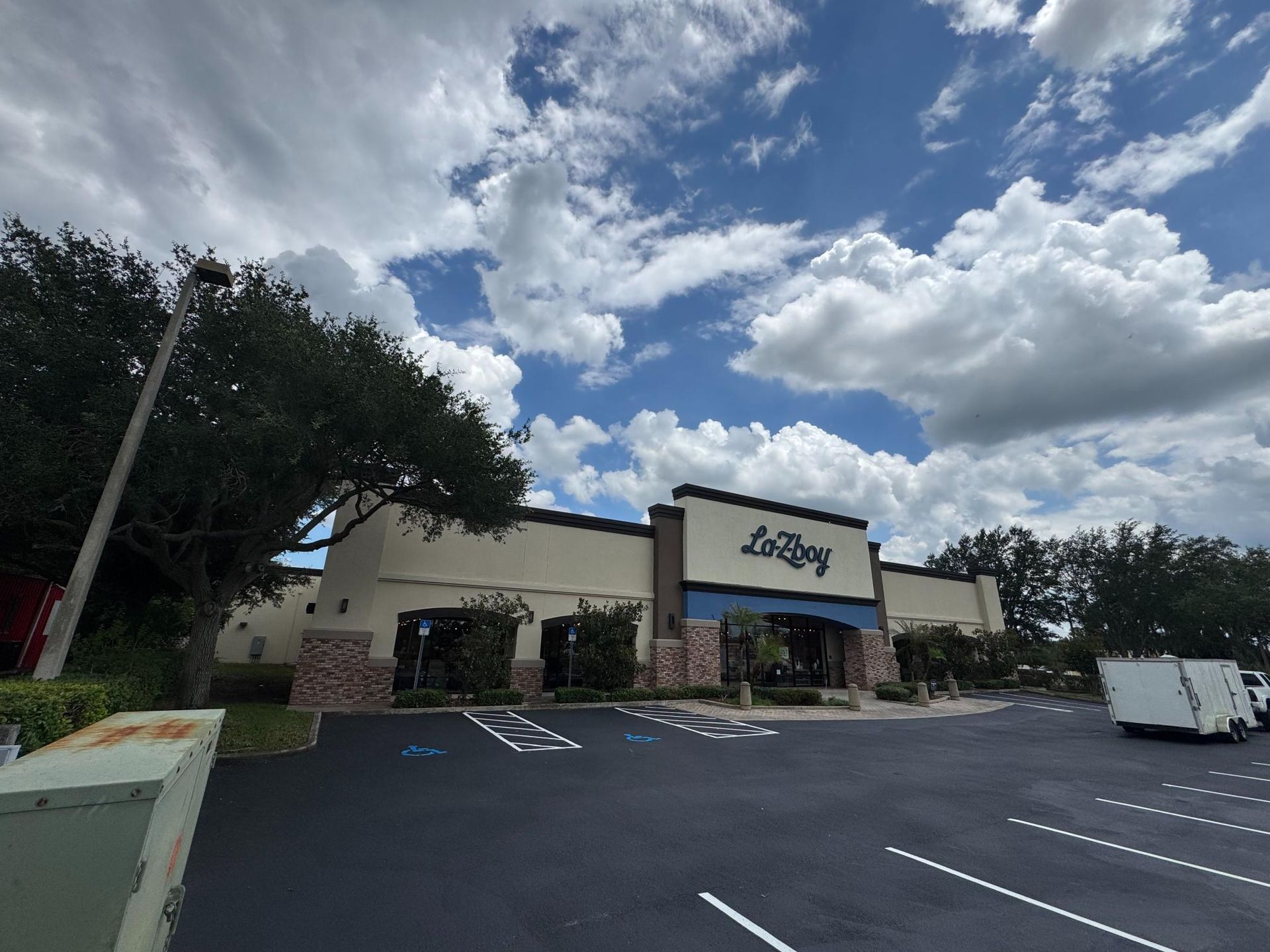 Strip mall storefront with parking lot under a cloudy sky, centered on a beige building with a blue sign.