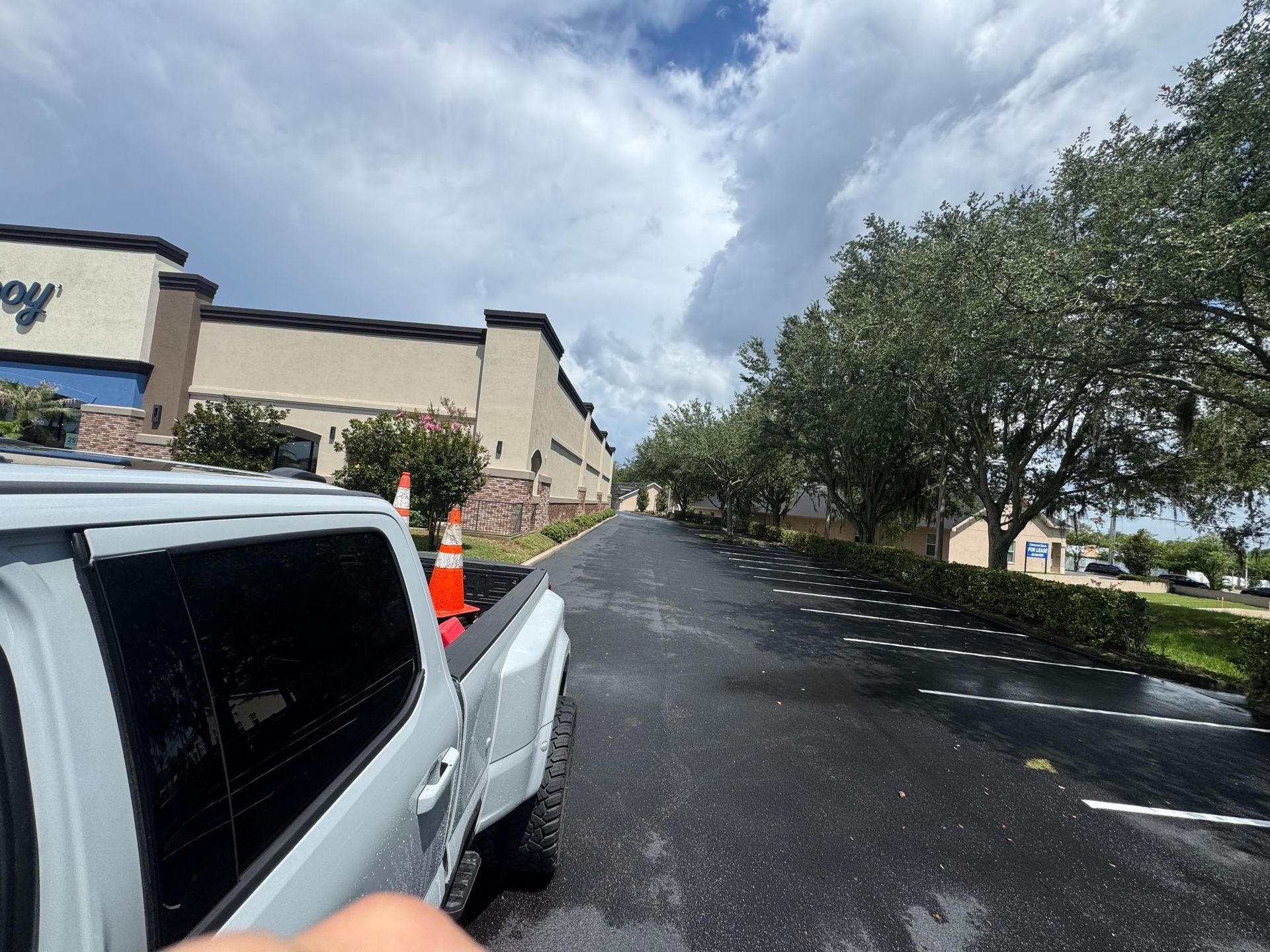 Wet parking lot beside a white truck and storefront under cloudy sky
