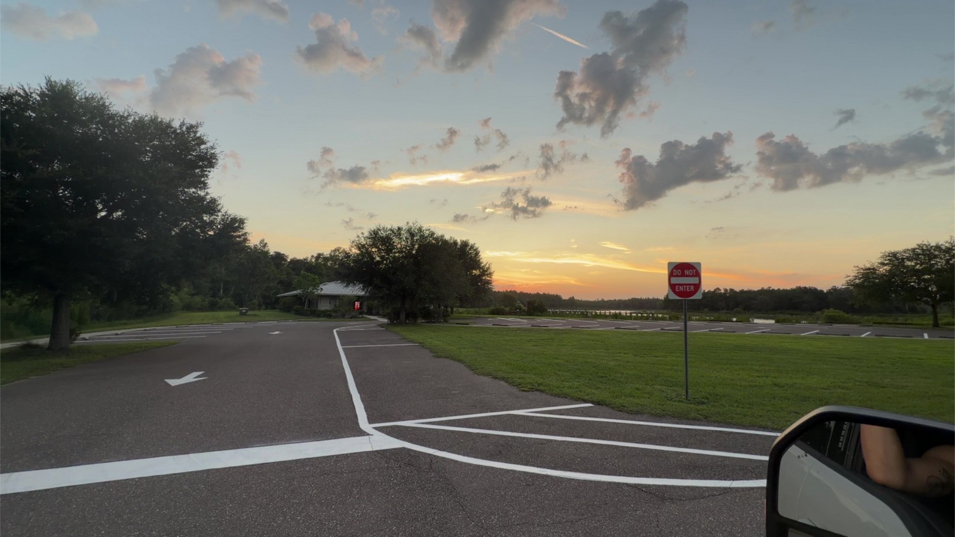 Sunset over a quiet road junction with a stop sign, grassy field, and trees under cloudy sky