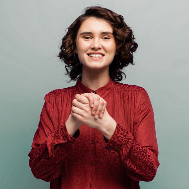 A woman in a red shirt is doing BSL and smiling.
