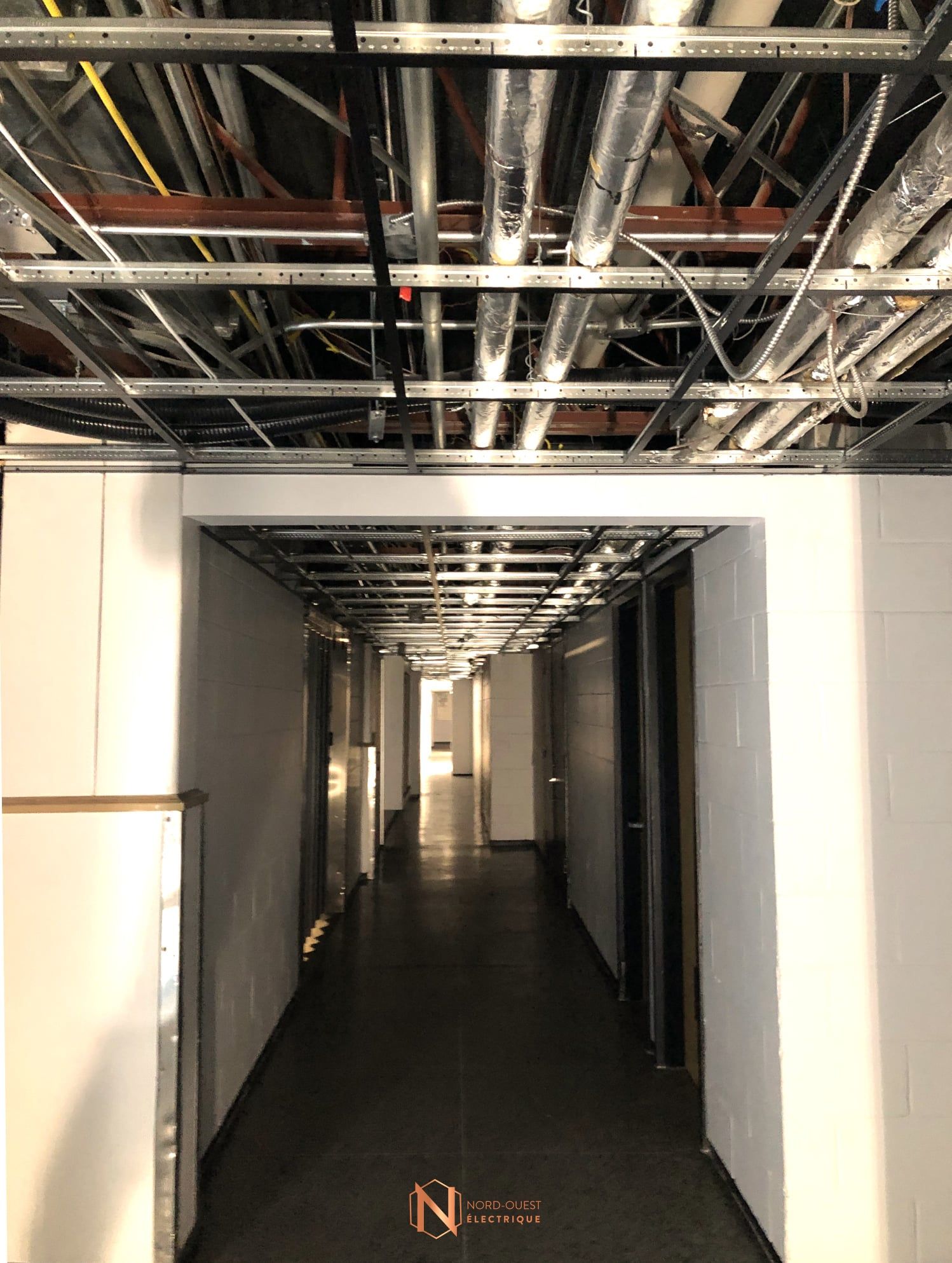 Un long couloir avec des tuyaux suspendus au plafond.