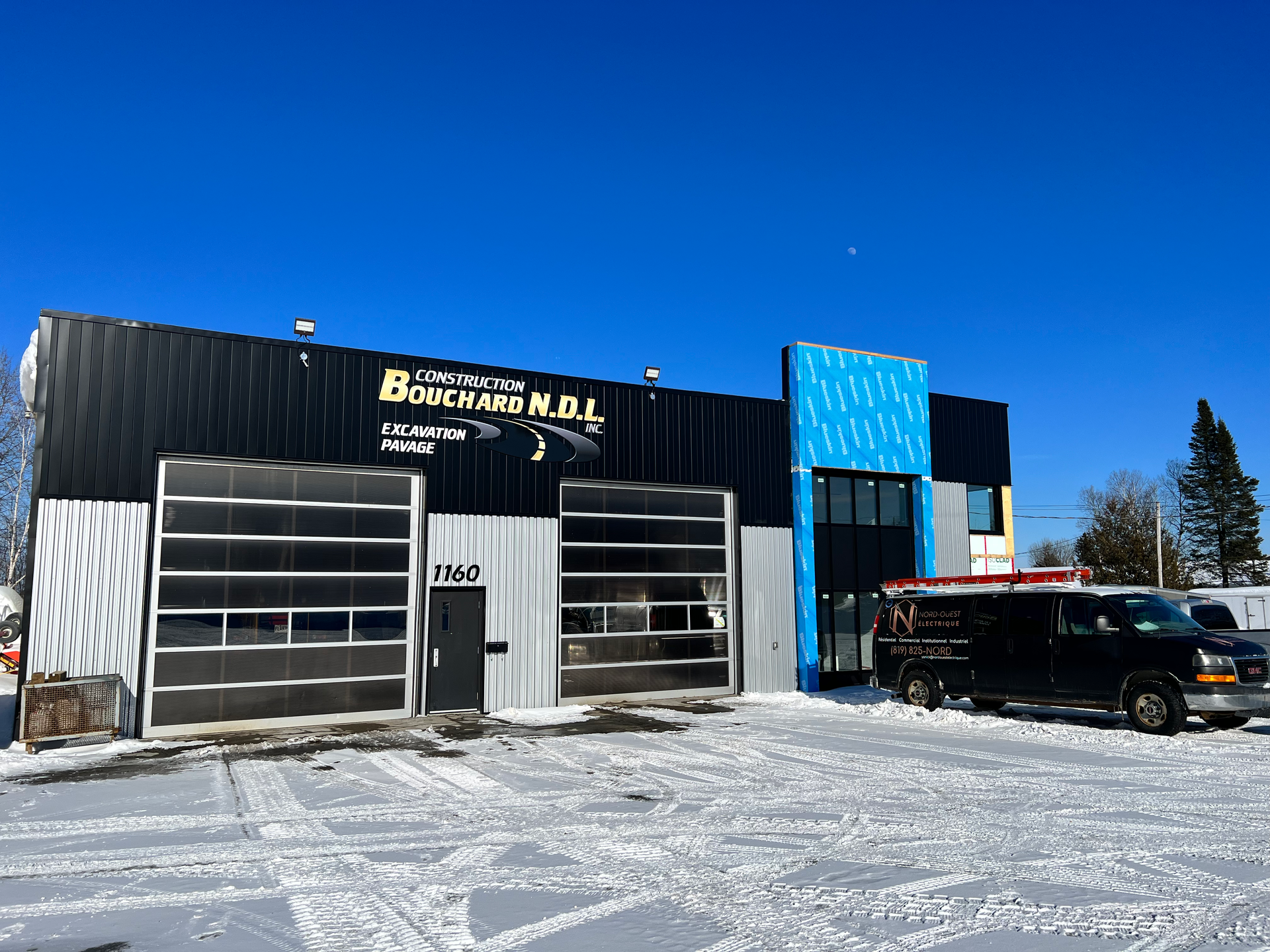 Une camionnette noire est garée devant un bâtiment sous la neige.
