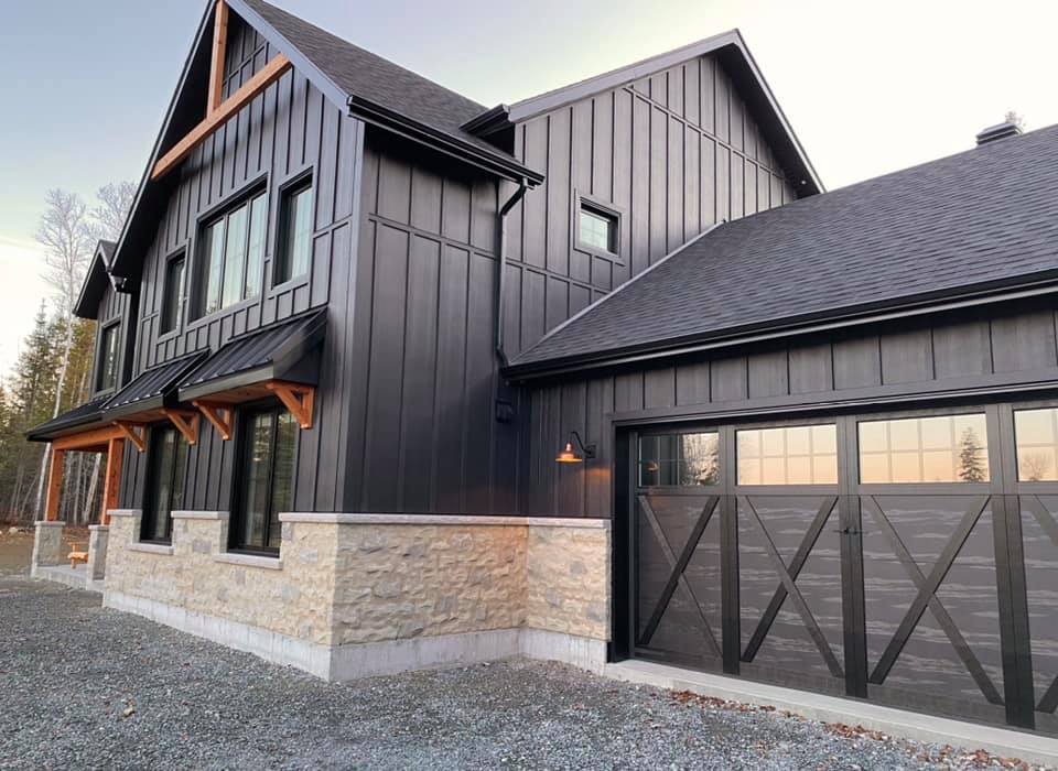 Une grande maison noire avec un garage à côté.
