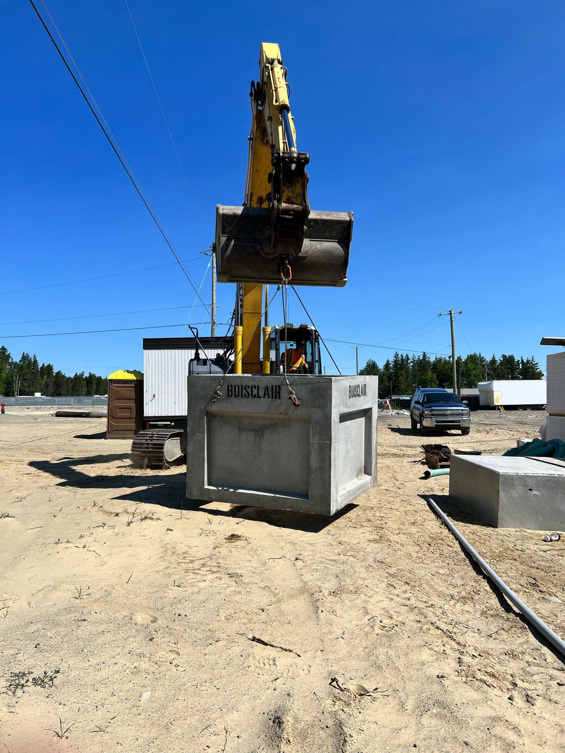 Une excavatrice jaune soulève un gros bloc de béton avec les lettres aisi dessus