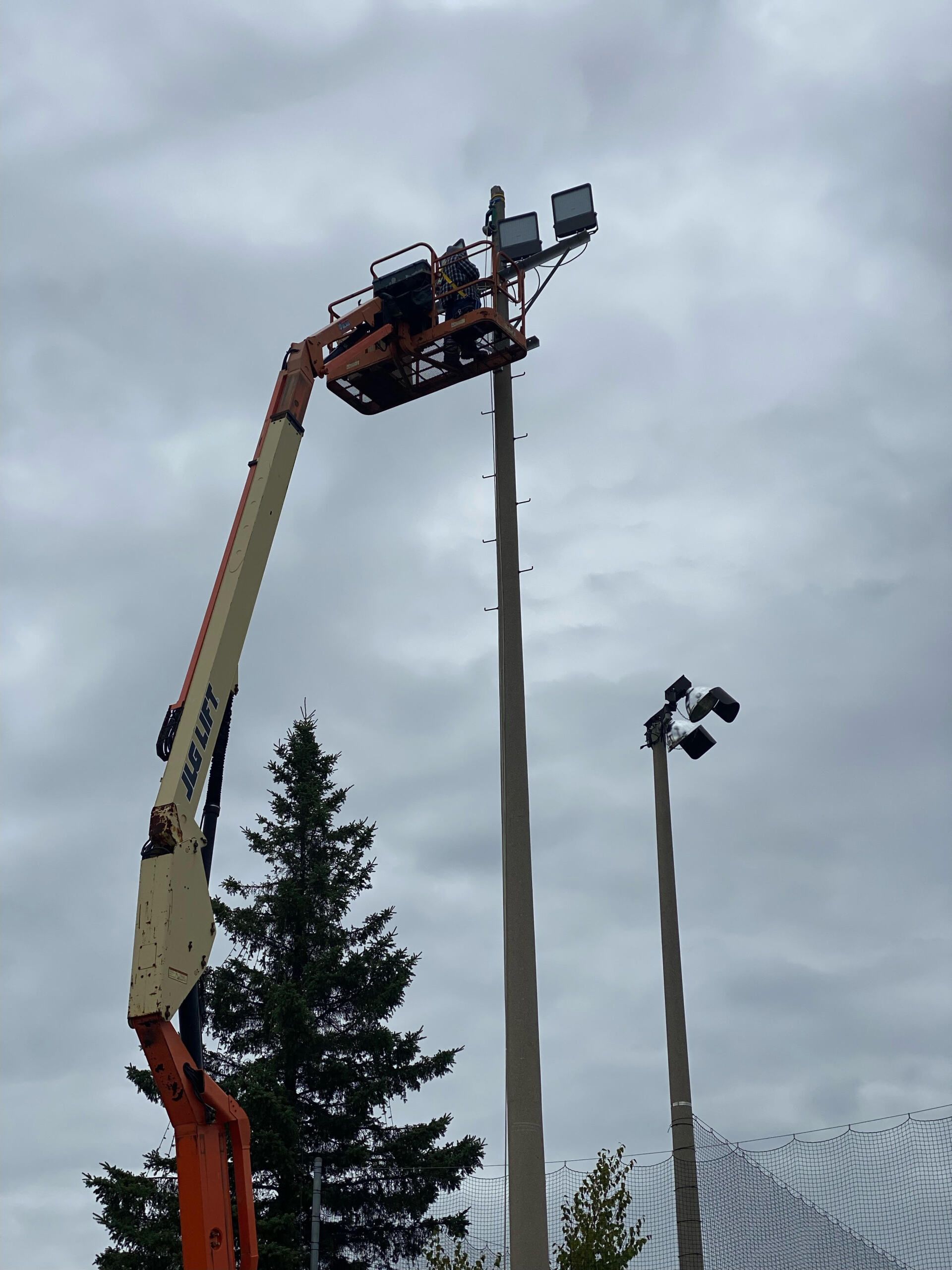 Une grue soulève un lampadaire avec un ciel nuageux en arrière-plan.