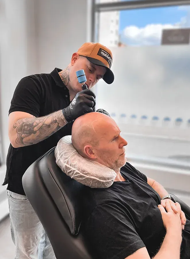 Barberare trimmar en skallig mans huvud i en salong, med nackstöd och svarta handskar