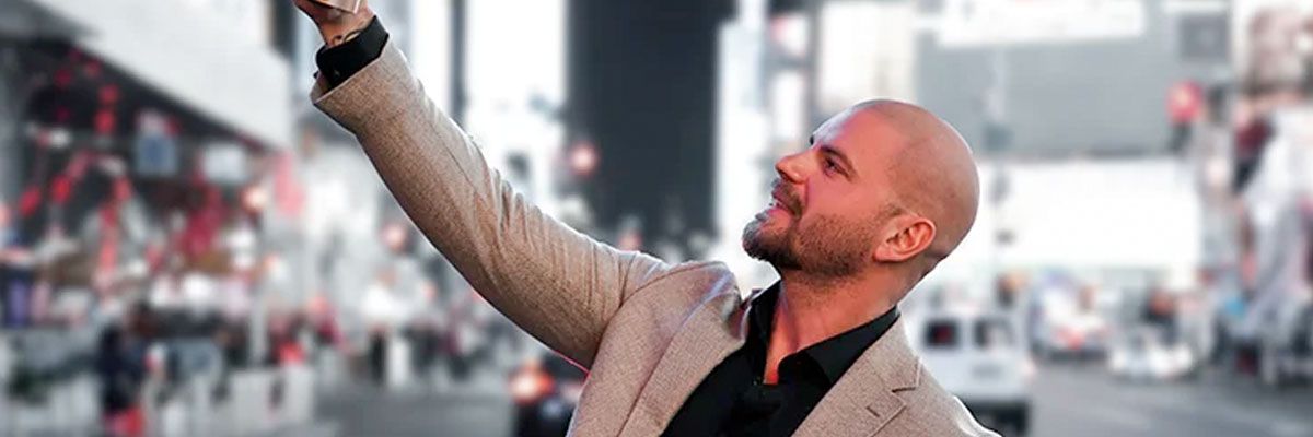 Man tar en selfie på ett evenemang, ler och höjer armen framför en suddig publik och scenbakgrund