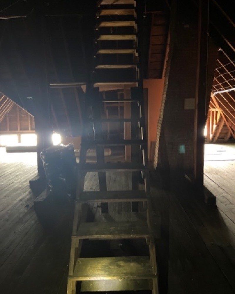 A steep wooden staircase leads upward into a dimly lit, unfinished attic space with wooden rafters.