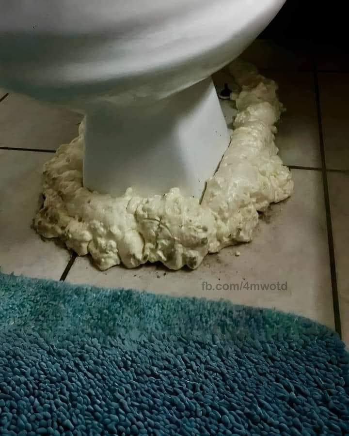 A toilet base improperly sealed to a tiled floor with expanding yellow spray foam.