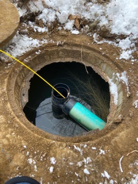 A yellow cable enters an open underground concrete pipe junction surrounded by dirt and light snow.