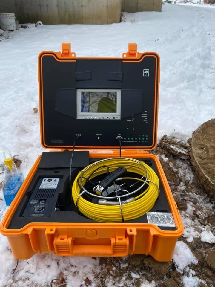 An orange industrial sewer inspection camera system in an open carrying case, sitting on snow-covered ground.