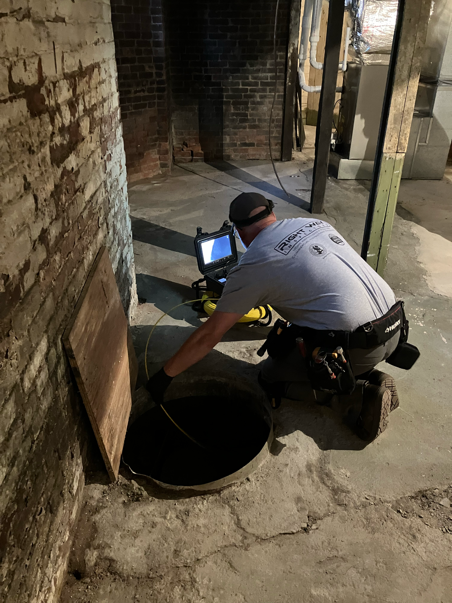 A technician inspects a dark, underground pipe in a brick basement using a portable camera monitor.