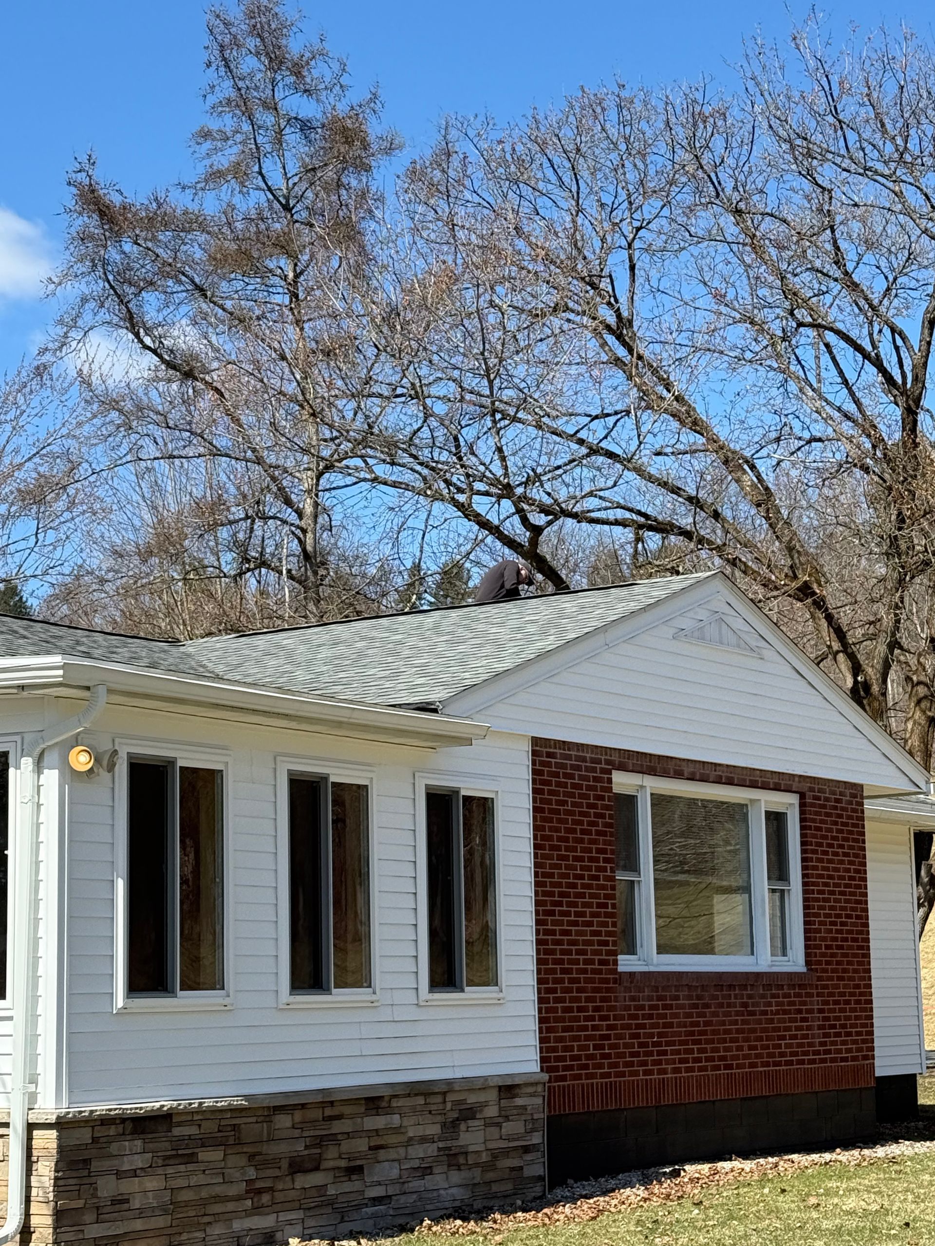 A one-story house with white siding, a brick facade section, stone-look foundation, and a gabled roof under a blue sky.