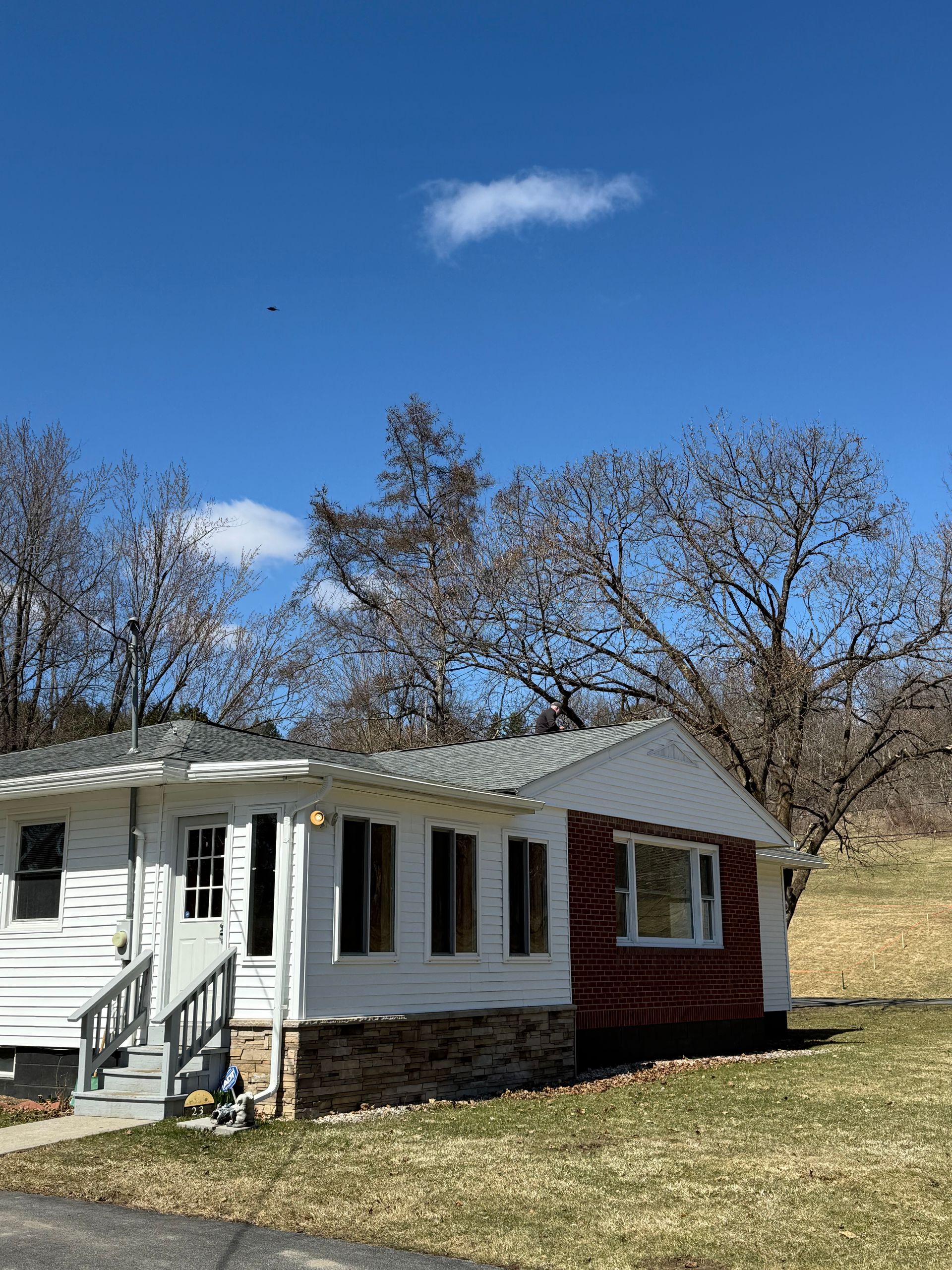 A white cottage with a brick accent wall, stone foundation, and small front porch sits under a bright blue sky.
