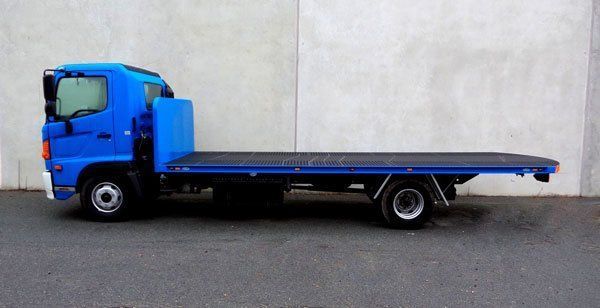 A Blue Flatbed Tow Truck Is Parked in Front of A White Wall — Welshpool, WA — PTE Group Pty Ltd