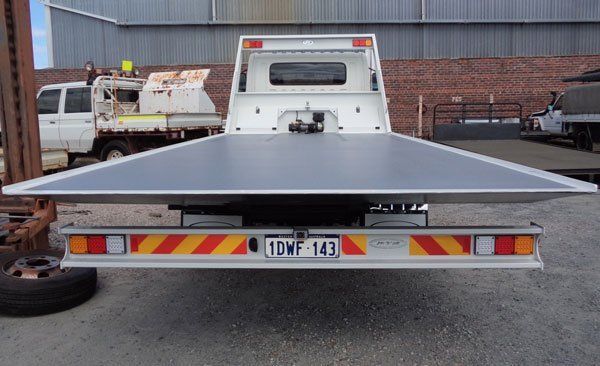 A Tow Truck with A Flat Bed Is Parked in Front of A Brick Building — Welshpool, WA — PTE Group Pty Ltd