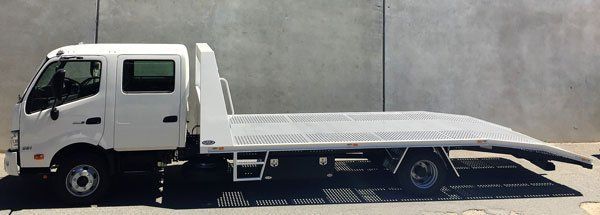 A White Tow Truck with A Flat Bed Is Parked in Front of A Concrete Wall — Welshpool, WA — PTE Group Pty Ltd