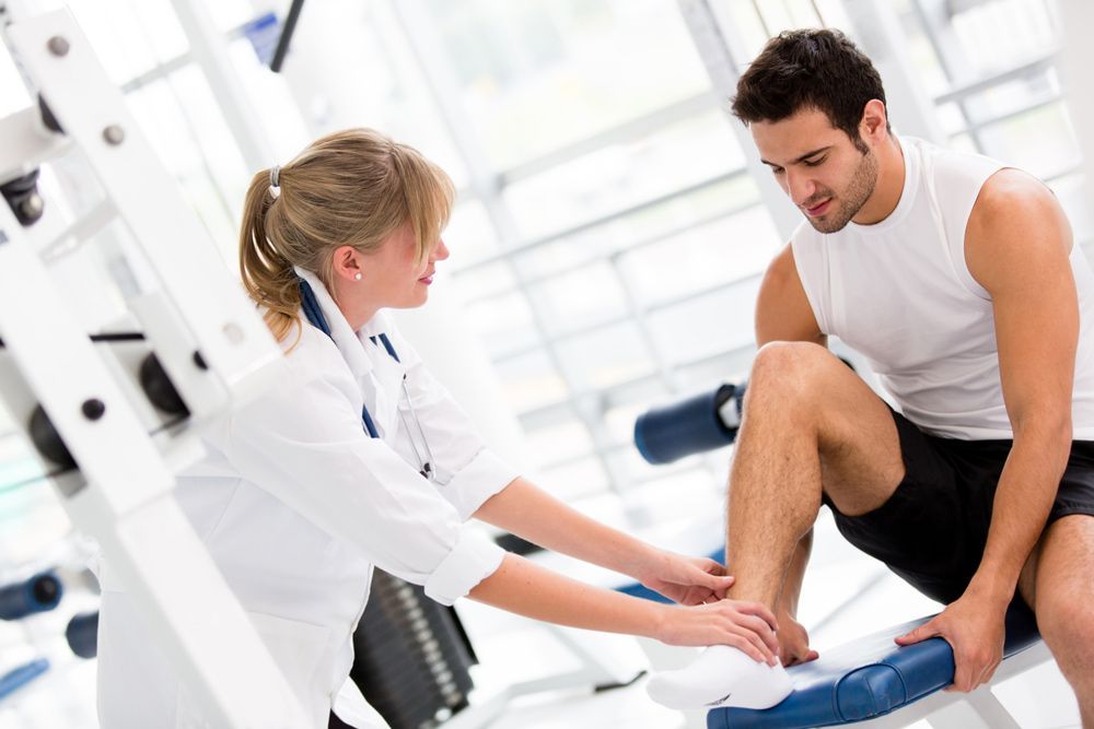 A Man Is Sitting On A Bench While A Nurse Examines His Leg — Caves Coastal Physiotherapy in Caves Beach, NSW