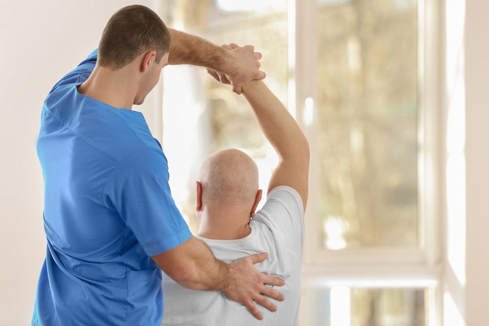 A Man Is Being Helped By A Nurse To Stretch His Arms — Caves Coastal Physiotherapy in Caves Beach, NSW