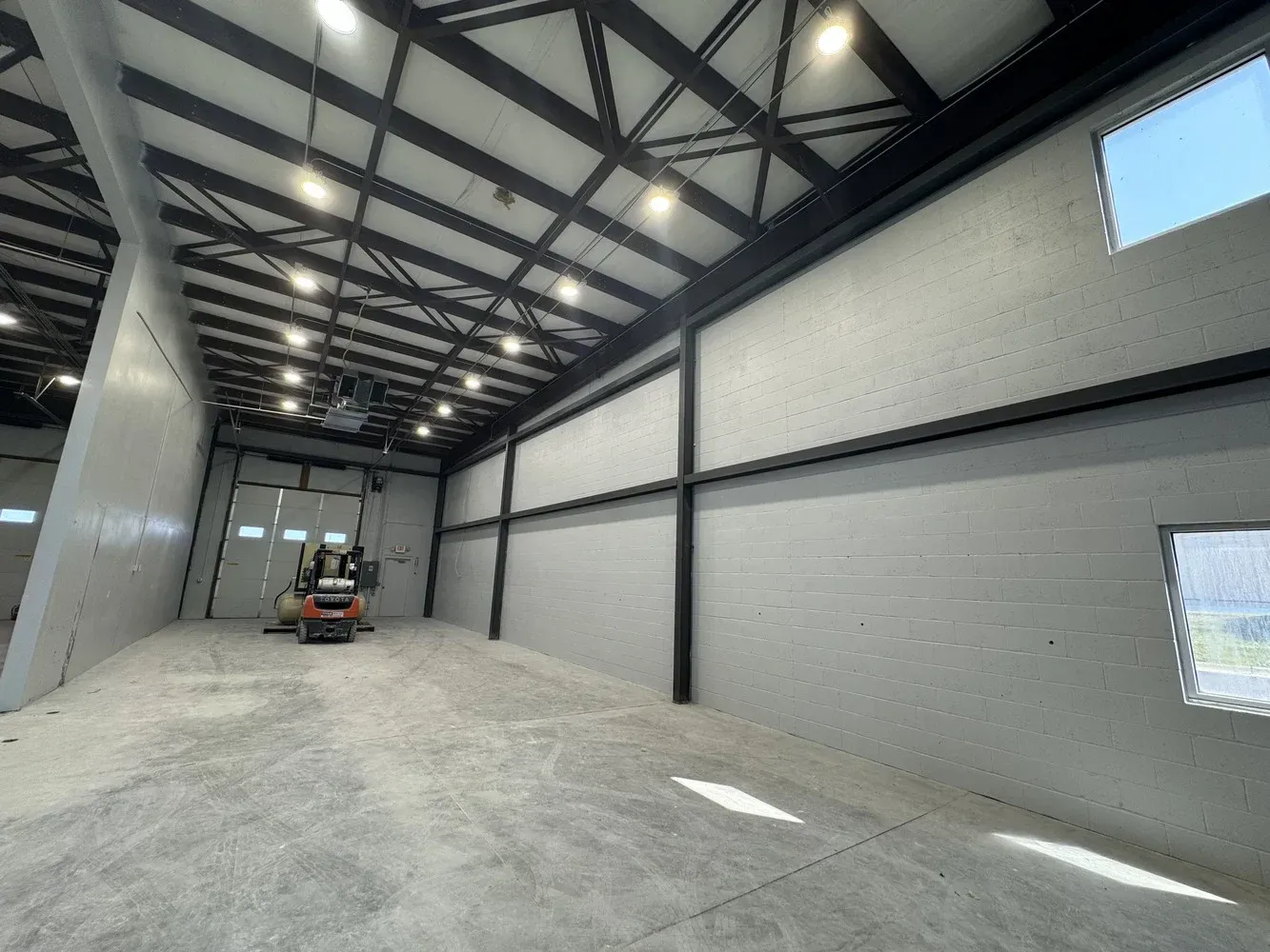 Large empty warehouse interior with steel beams, high ceiling lights, and a small forklift near the back