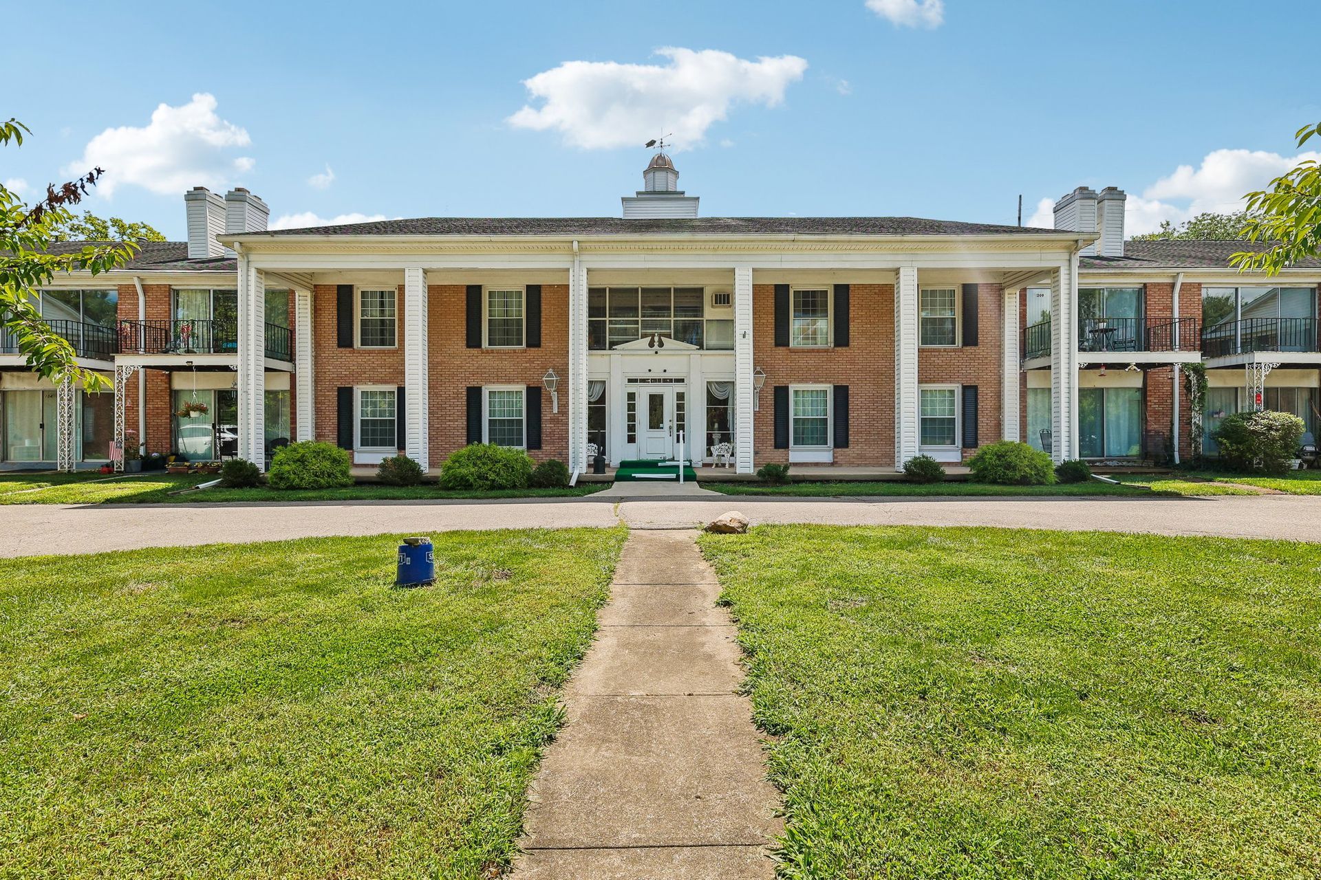 Photo of an apartment building in the colonial revival style, showing two stories with a walkway and driveway out front