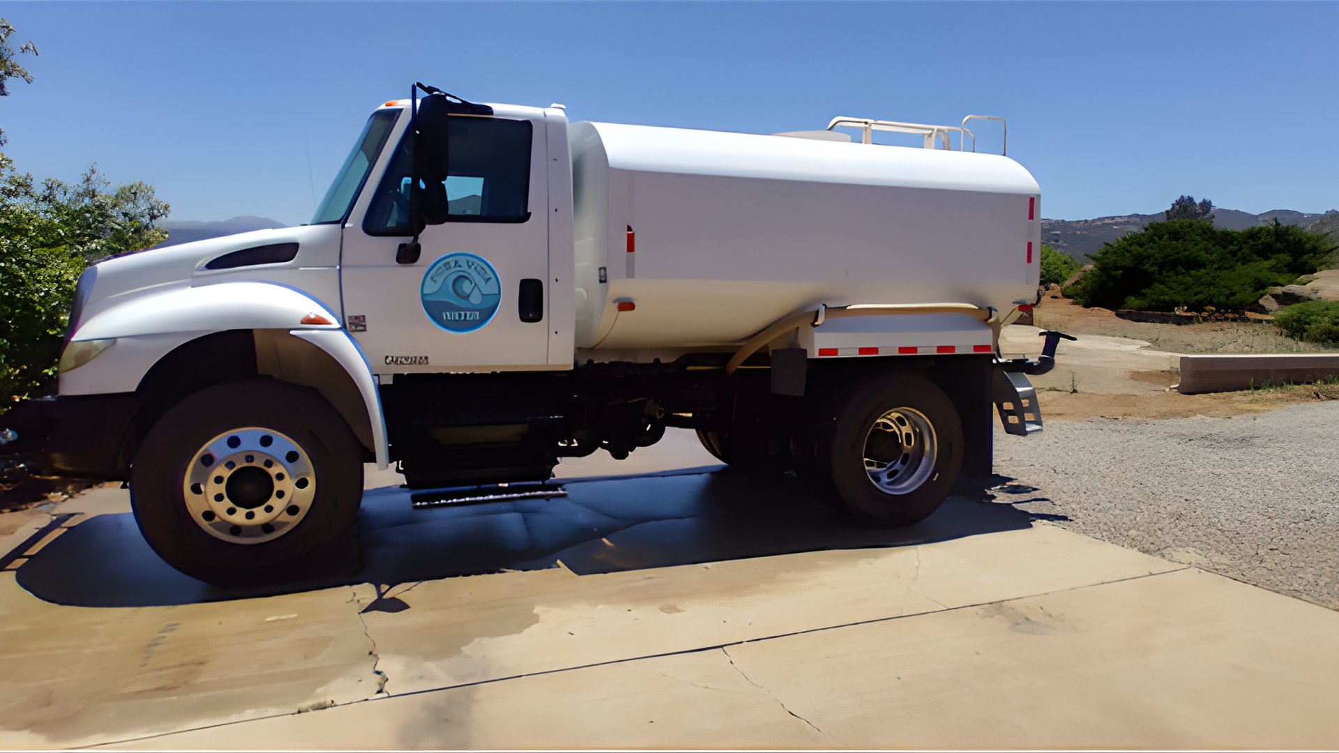 A white water truck parked on a concrete driveway against a clear blue sky.