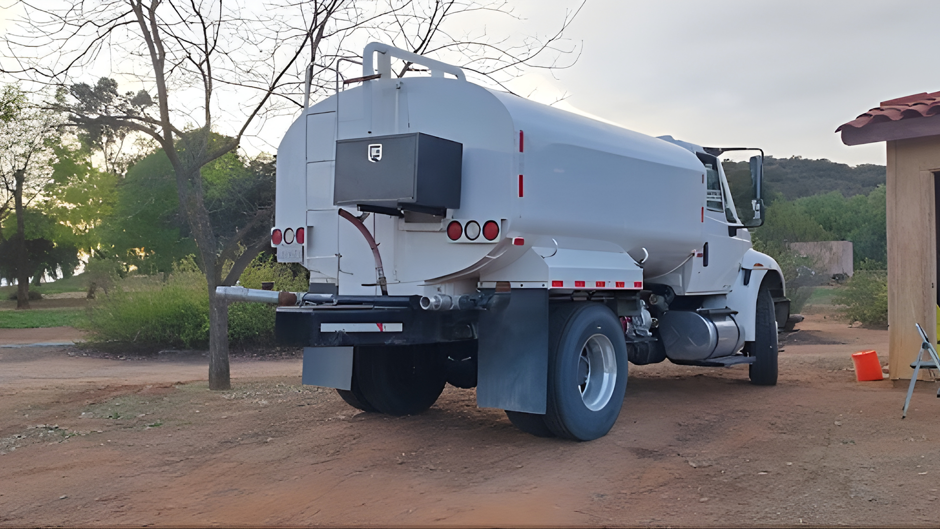 A white water tanker truck parked on a dirt lot during sunset.