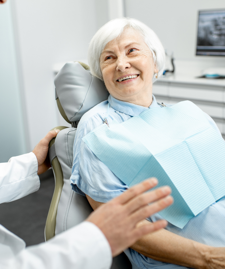 An elderly woman is smiling while sitting in a dental chair.