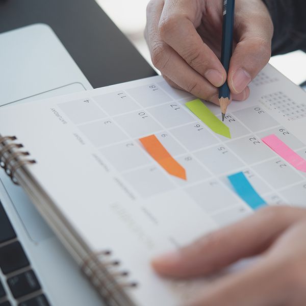 Hand writing on a colorful paper calendar with highlighted dates and a spiral binding