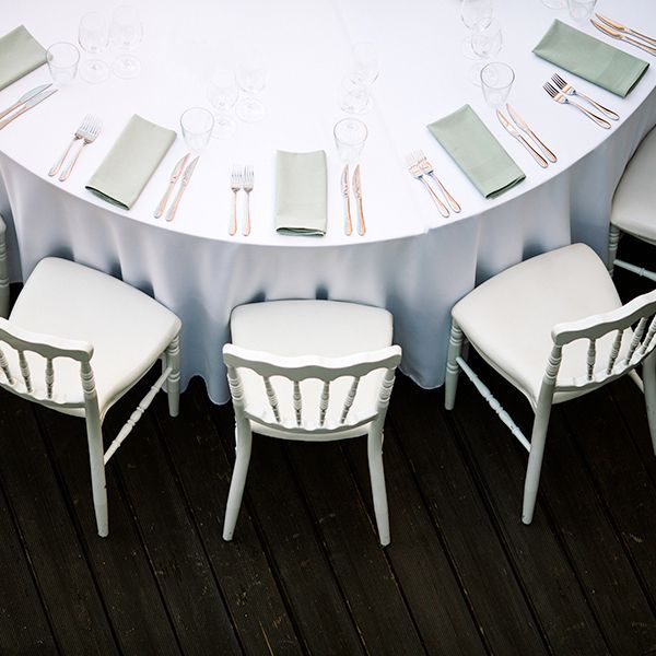 Round dining table set with white chairs, pale blue tablecloth, and neatly arranged napkins and glassware