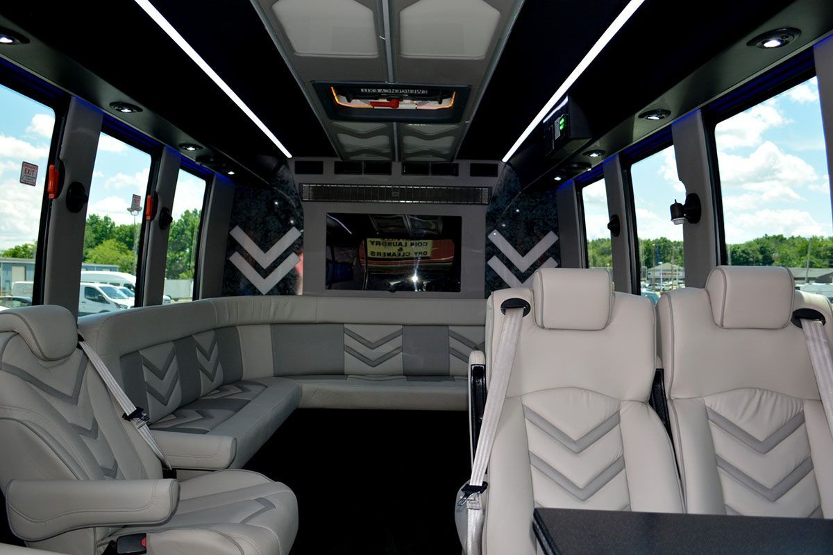 Luxury van interior with white leather seats, panoramic windows, and a rear entertainment screen