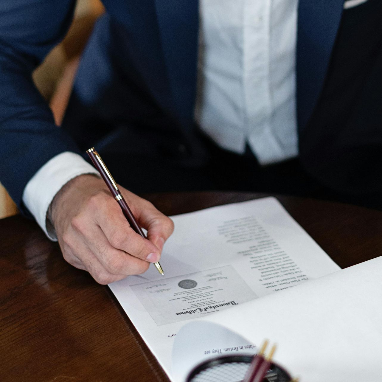 Person in suit signs legal document with pen at a desk.