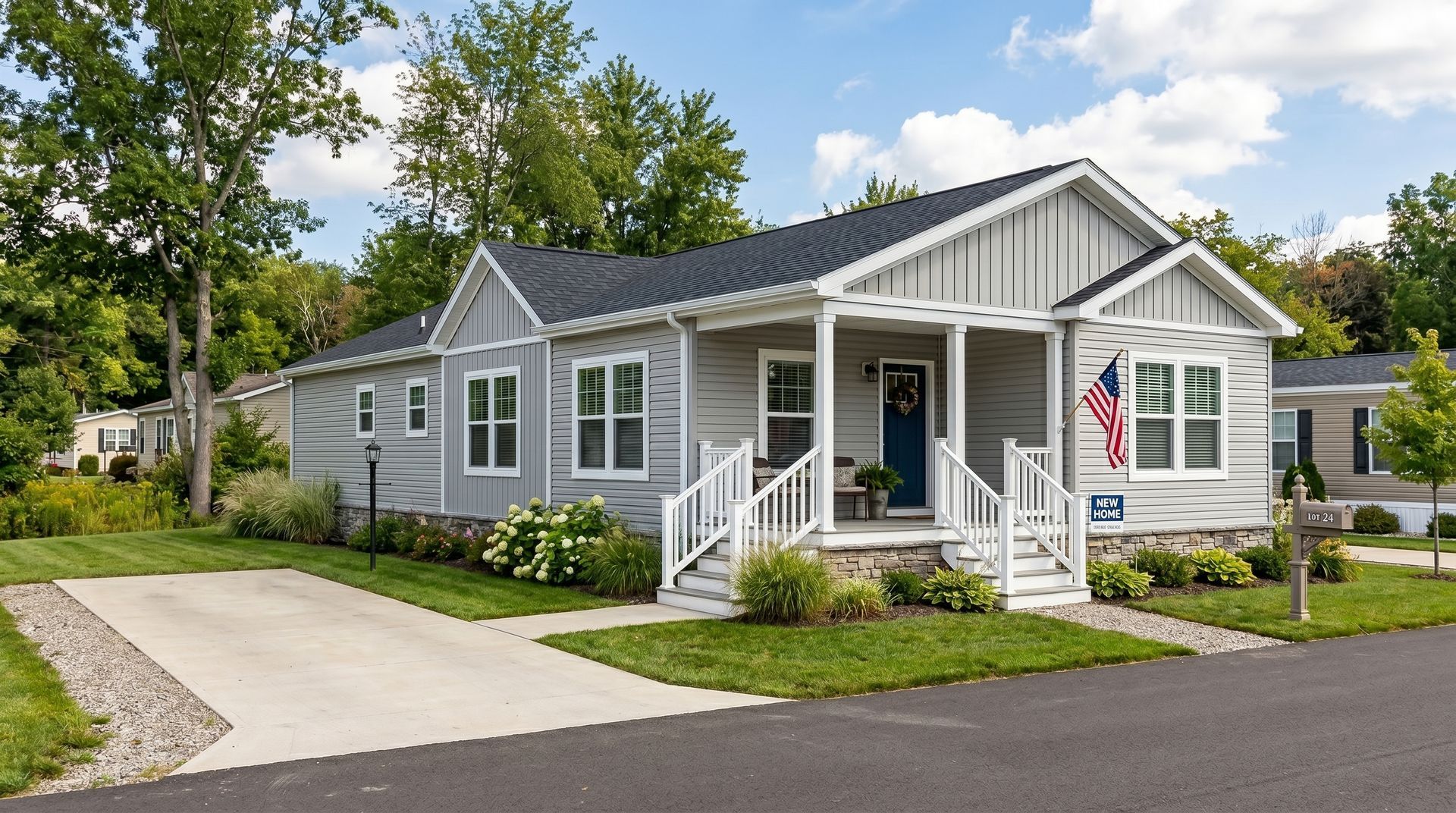 Gray house with white trim and porch, driveway, lawn, and trees on a sunny day