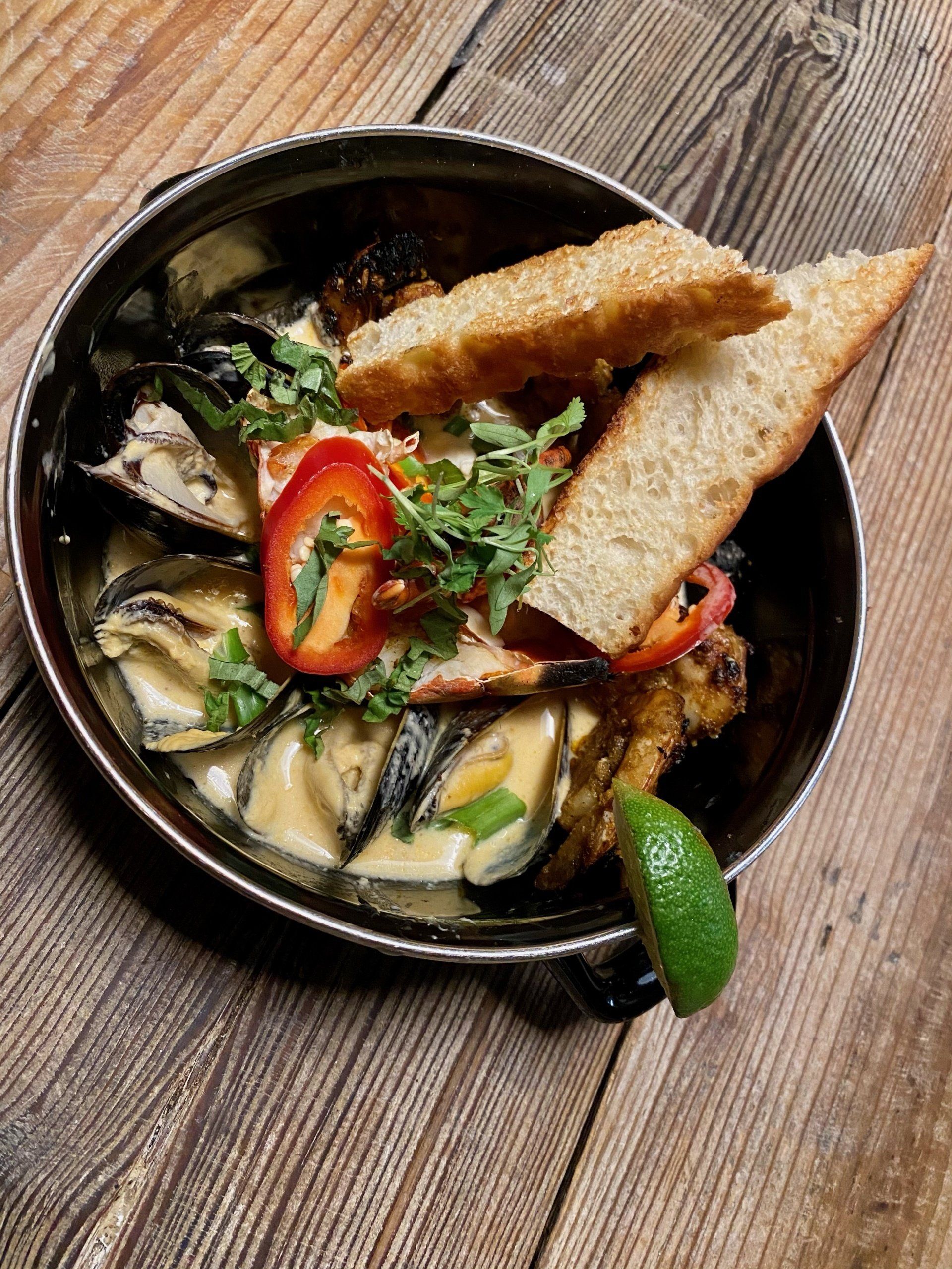 a bowl of food with bread and vegetables on a wooden table