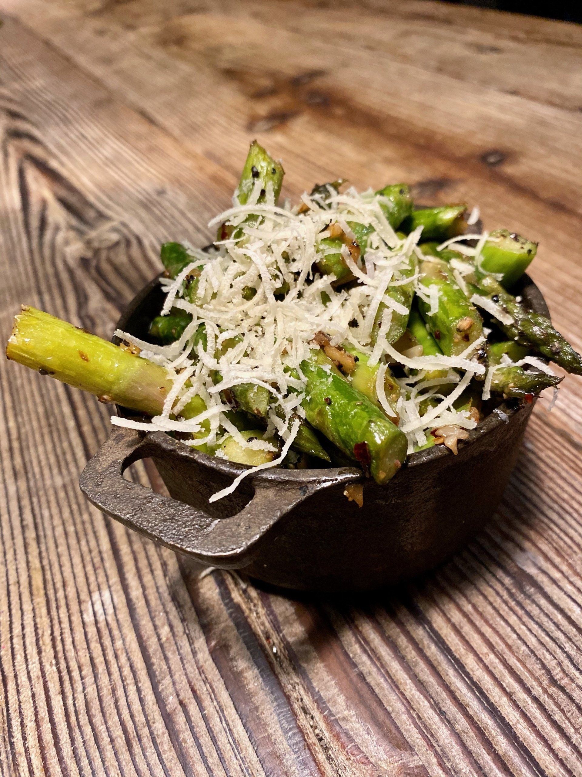 a bowl of asparagus and cheese on a wooden table