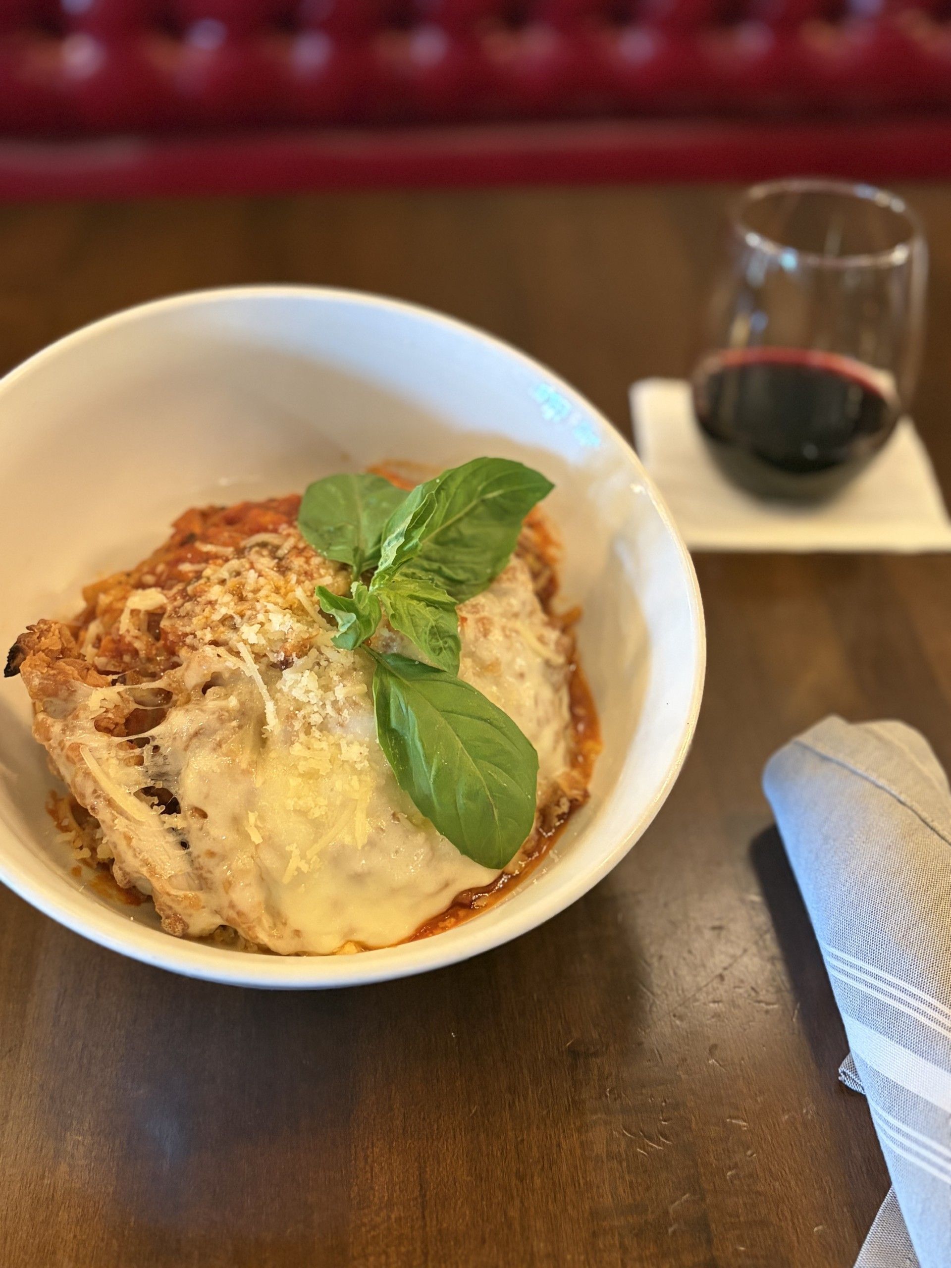Breaded chicken breast, housemade marinara, linguine noodles, garnished with fresh grated Parmesan and basil.
, beside a glass of red wine on a table.