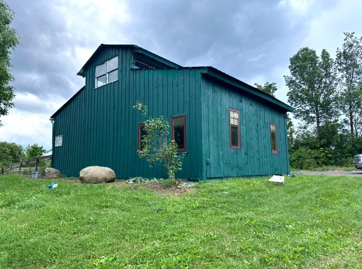 Barn painting services by Patrick Farm Painting in Boonville, New York. This image features a professionally restored barn or farmhouse surrounded by peaceful countryside scenery, open farmland, and natural outdoor lighting. The freshly painted siding, trim, and exterior surfaces highlight the craftsmanship of experienced barn painters and the trusted farm painting guy from Patrick Farm Painting, a company that paints barns in New York. The building appears clean, durable, and visually refreshed with smooth finishes and vibrant color restoration. This detailed description helps visually impaired website visitors imagine the rural setting, the scale of the agricultural structure, and the quality transformation completed during the farm painting project.