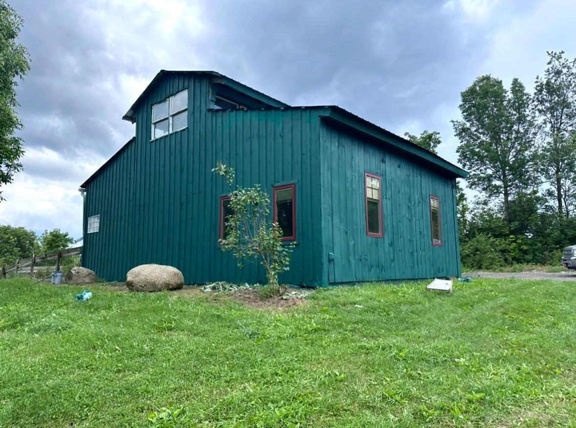 Barn painting services by Patrick Farm Painting in Norwich, New York. This image features a restored rural barn or farmhouse surrounded by open countryside, green grass, and natural outdoor lighting. The freshly painted exterior highlights the detailed craftsmanship of experienced barn painters and the trusted farm painting guy from Patrick Farm Painting, a company that paints barns in New York. The siding, trim, and exterior surfaces appear clean, vibrant, and professionally coated, creating a vivid before-and-after transformation. This detailed description helps visually impaired website visitors imagine the peaceful farm setting, the scale of the building, and the quality of the completed farm painting project.
