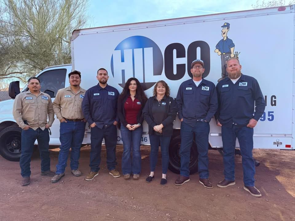 Group of people in work attire standing in front of a white truck with a company logo.