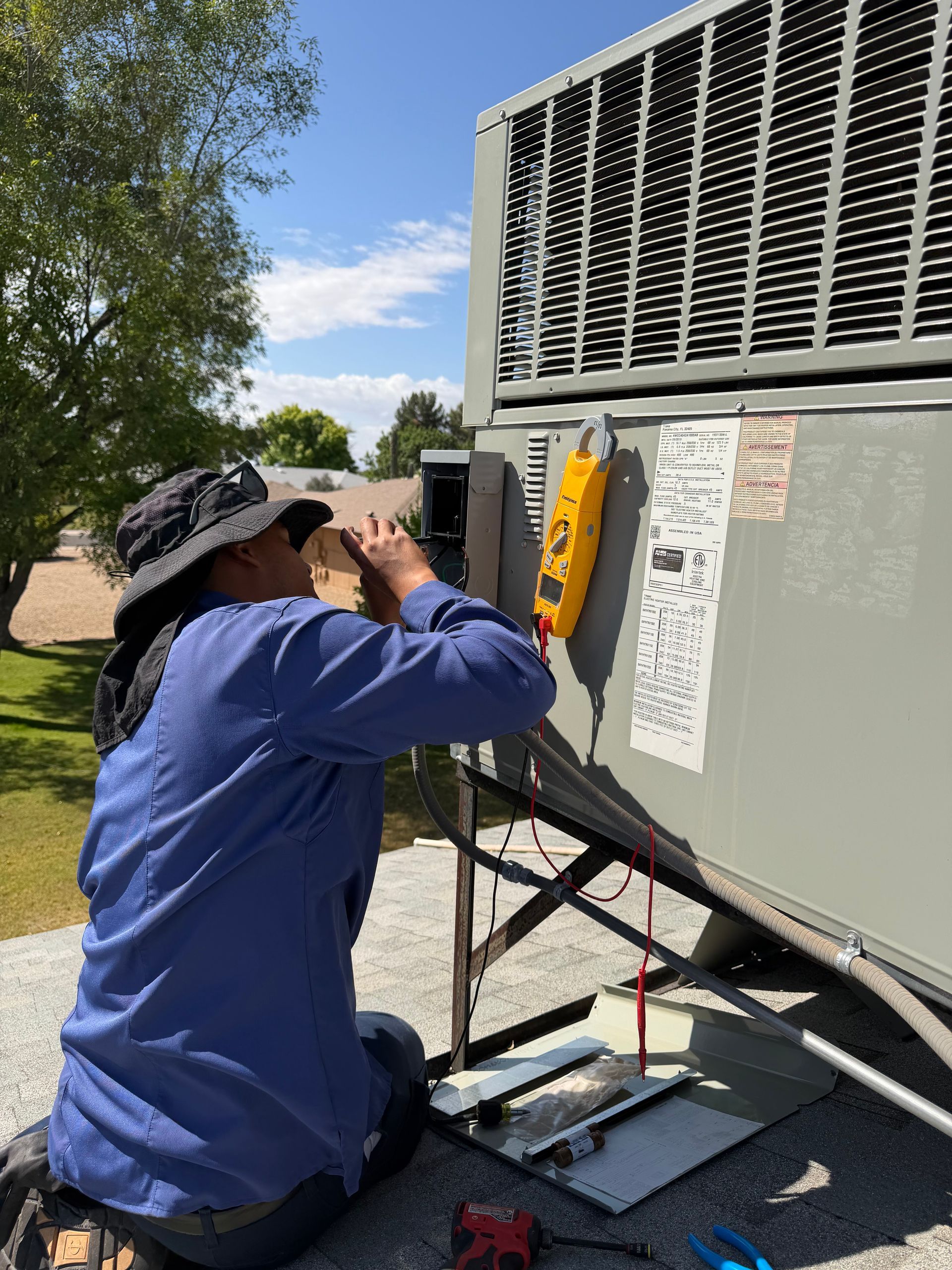 Worker in blue shirt inspecting HVAC unit with a gauge outdoors