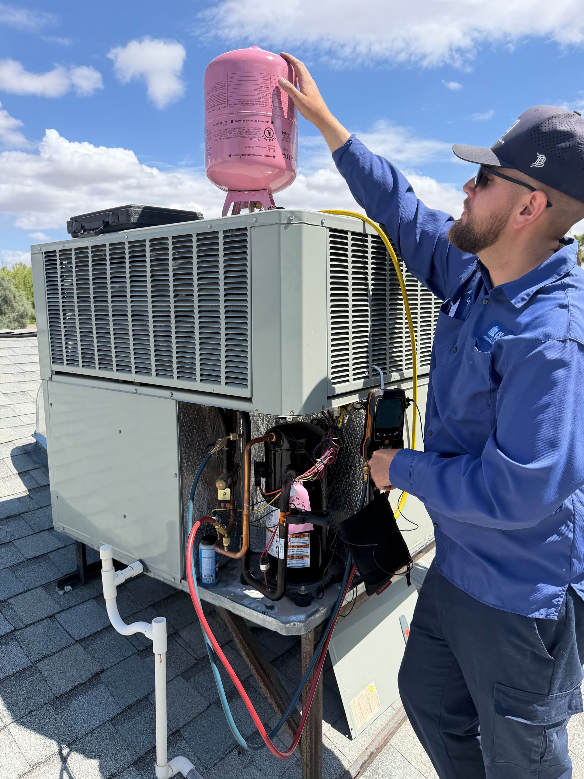 Technician checking rooftop HVAC unit with a pink refrigerant tank on top