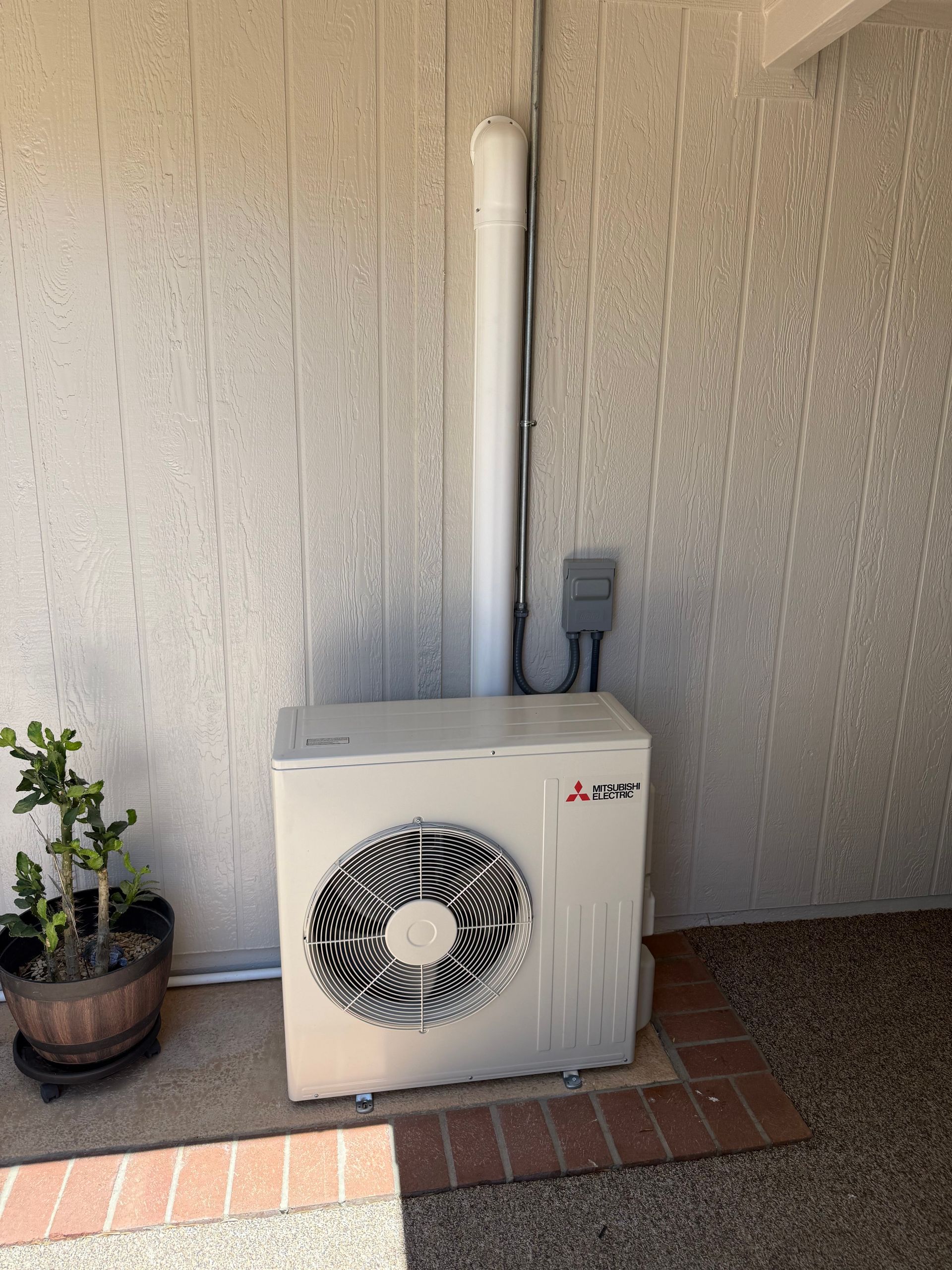 Outdoor air conditioner unit beside a stucco wall and potted plant on a brick patio