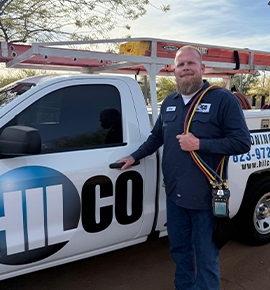 Man in work clothes stands by a white pickup truck with company logo. He holds gauges.