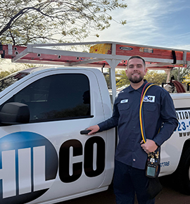 HVAC technician stands by work truck, holding tools.