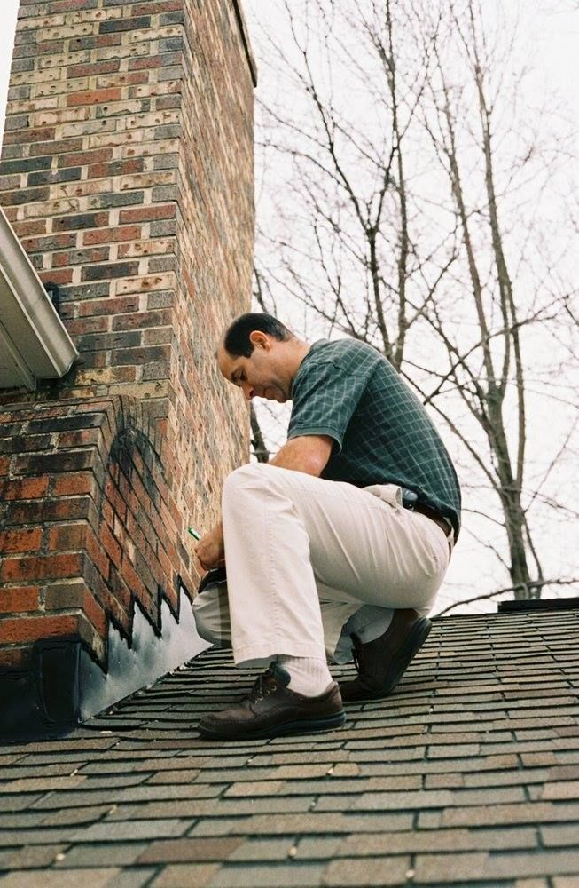 Man on a roof near a brick chimney, examining flashing.