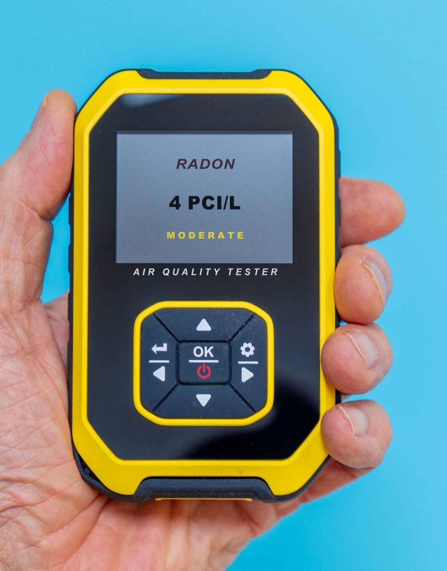Hand holding an air quality tester displaying a radon level of 4 pCi/L, labeled