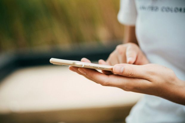 Person holding and tapping a smartphone with blurred outdoor background.