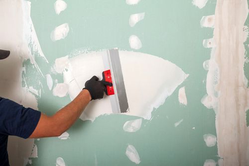 Person using a putty knife to spread drywall compound on a wall, covering screw holes.